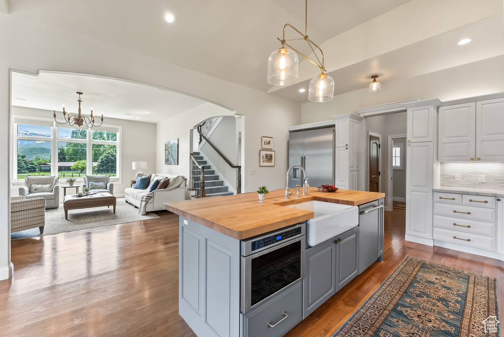 Kitchen featuring tasteful backsplash, a center island with sink, butcher block counters, hardwood / wood-style flooring, and white cabinetry