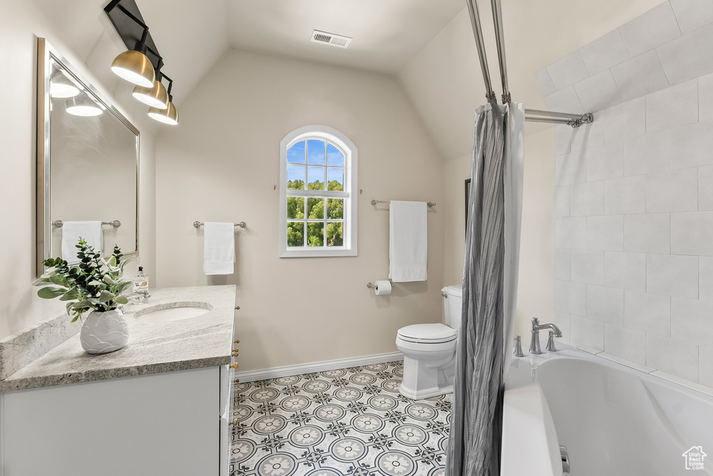 Bathroom with a bath to relax in, oversized vanity, toilet, tile floors, and lofted ceiling