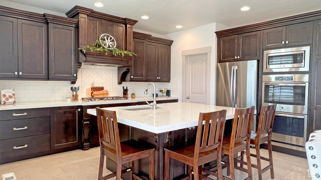 Kitchen featuring light tile flooring, stainless steel appliances, backsplash, dark brown cabinets, and sink