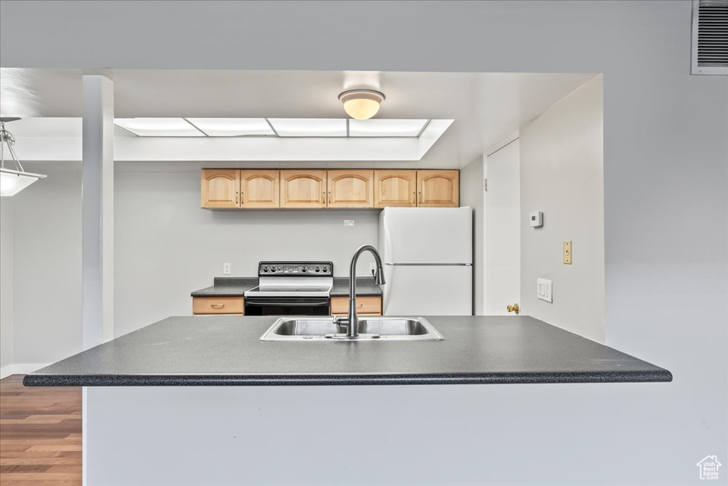 Kitchen with hardwood / wood-style floors, white fridge, light brown cabinetry, sink, and electric range oven