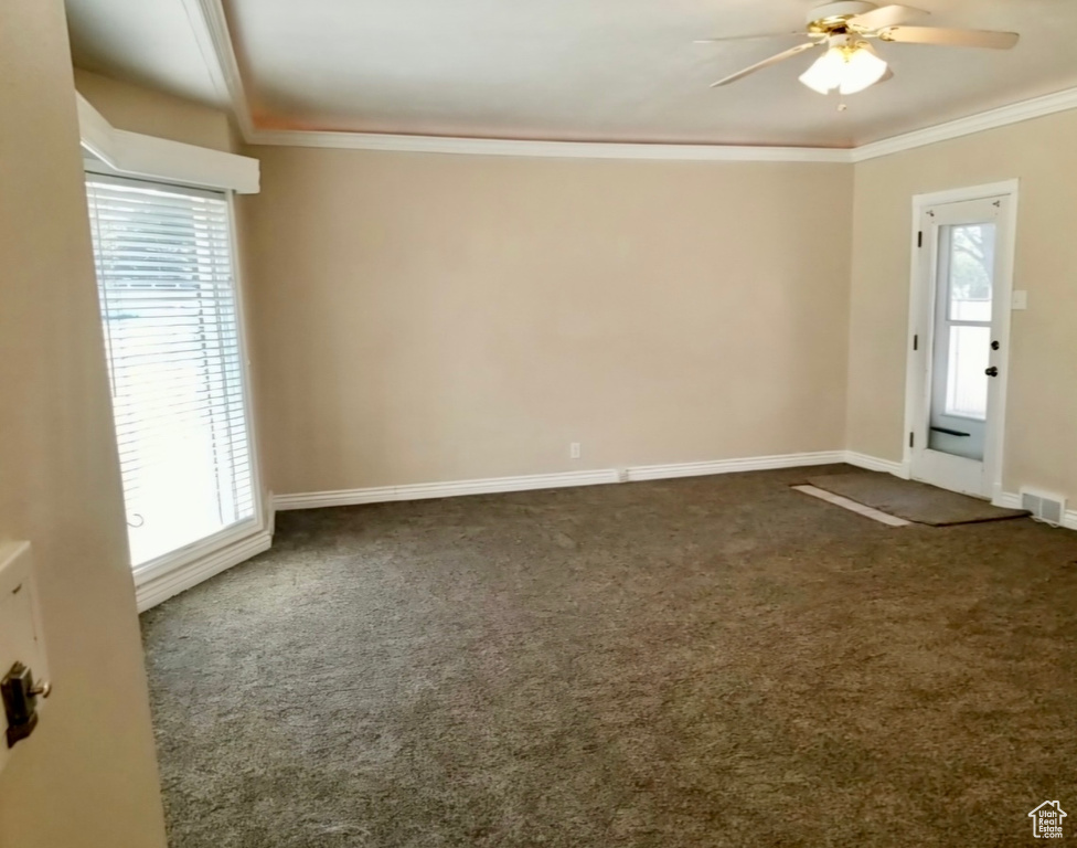 Empty room with ceiling fan, plenty of natural light, and dark colored carpet