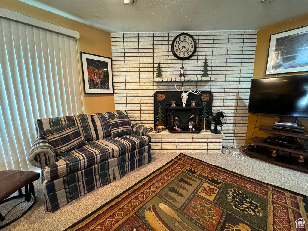 Living room with carpet flooring, brick wall, a textured ceiling, and a fireplace