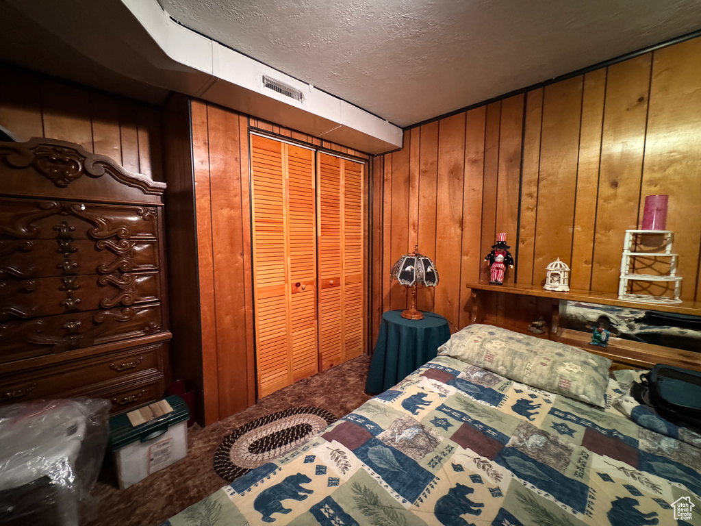 Bedroom featuring carpet, wooden walls, a closet, and a textured ceiling