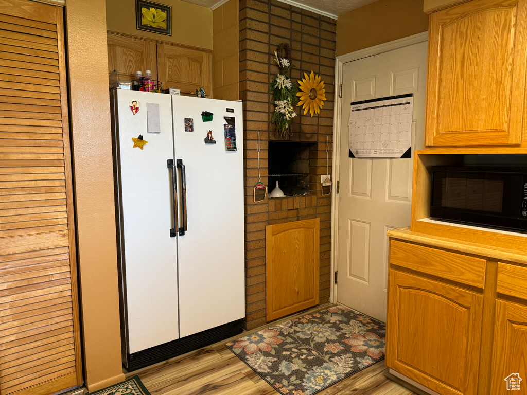 Kitchen with light hardwood / wood-style flooring, white refrigerator, and black microwave