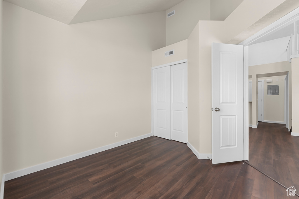 Unfurnished bedroom with a closet, dark hardwood / wood-style flooring, and a towering ceiling