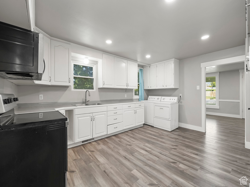 Kitchen with light hardwood / wood-style floors, electric range, sink, washer and clothes dryer, and white cabinetry