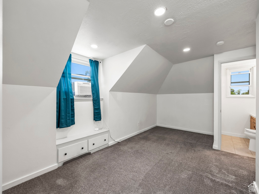 Additional living space with dark colored carpet, vaulted ceiling, and a textured ceiling