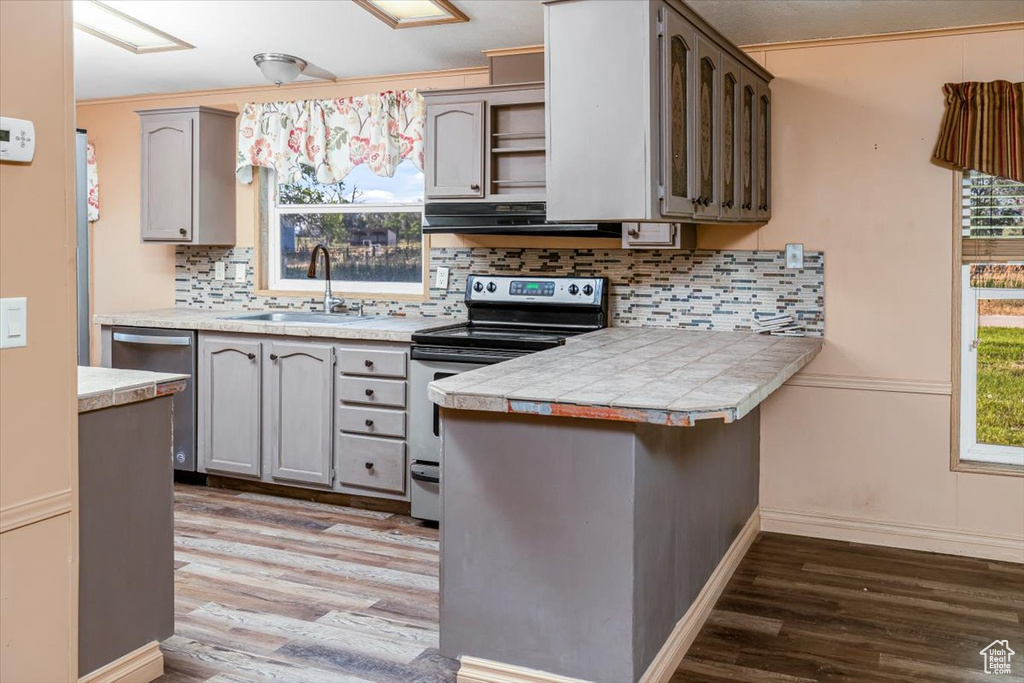 Kitchen featuring appliances with stainless steel finishes, hardwood / wood-style flooring, kitchen peninsula, extractor fan, and sink