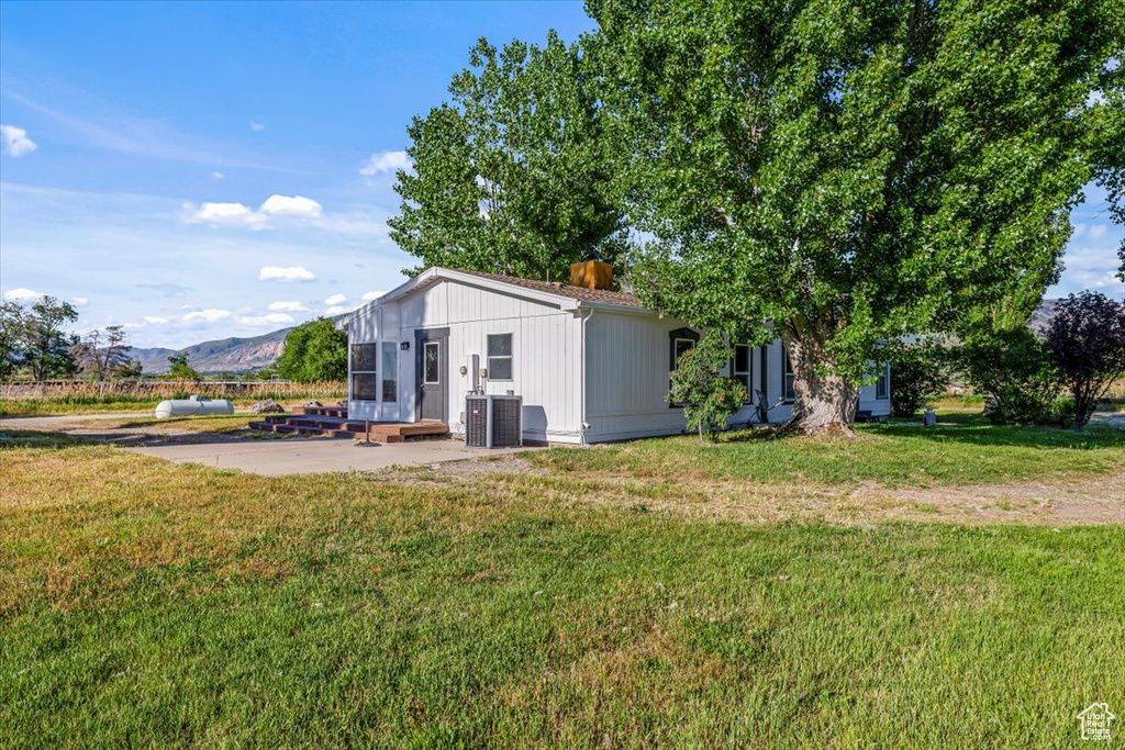 Exterior space with a patio area, a mountain view, central air condition unit, and a lawn