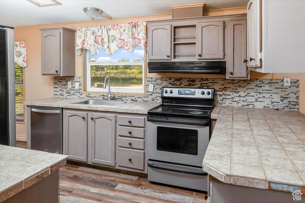 Kitchen featuring backsplash, extractor fan, wood-type flooring, sink, and appliances with stainless steel finishes