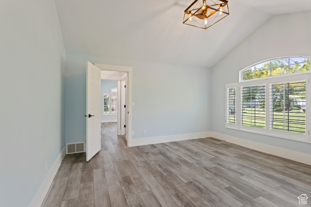 Empty room featuring a notable chandelier, high vaulted ceiling, plenty of natural light, and hardwood / wood-style flooring