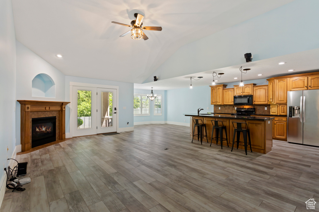 Kitchen with light hardwood / wood-style floors, black appliances, backsplash, a center island, and a kitchen bar