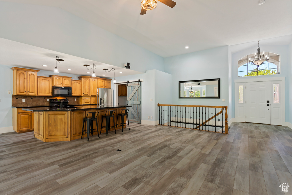 Kitchen featuring high vaulted ceiling, a center island with sink, black appliances, and hardwood / wood-style flooring