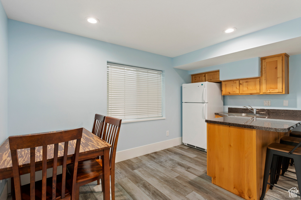 Kitchen with kitchen peninsula, white refrigerator, light wood-type flooring, sink, and a breakfast bar