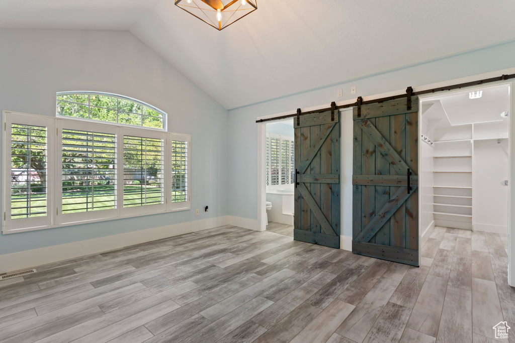 Unfurnished room with high vaulted ceiling, a barn door, and light hardwood / wood-style floors