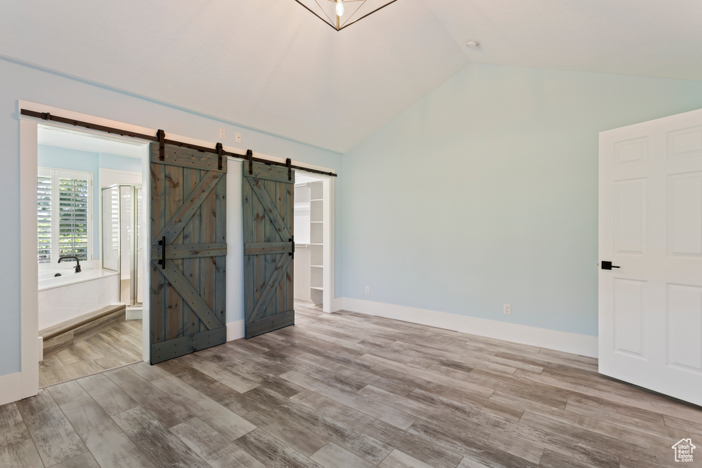 Unfurnished bedroom with ensuite bath, a barn door, vaulted ceiling, and hardwood / wood-style flooring