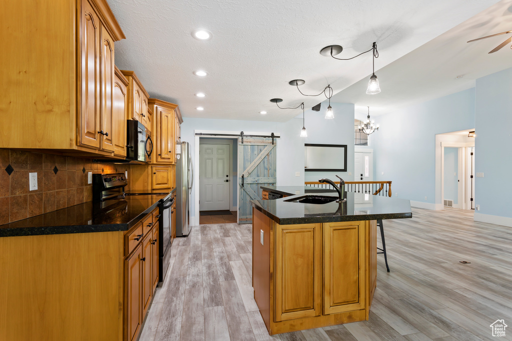 Kitchen with light hardwood / wood-style flooring, appliances with stainless steel finishes, an island with sink, backsplash, and a barn door