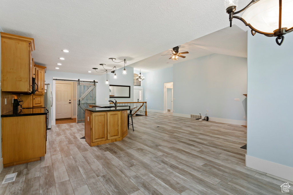 Kitchen featuring a center island with sink, a barn door, light hardwood / wood-style floors, and ceiling fan with notable chandelier