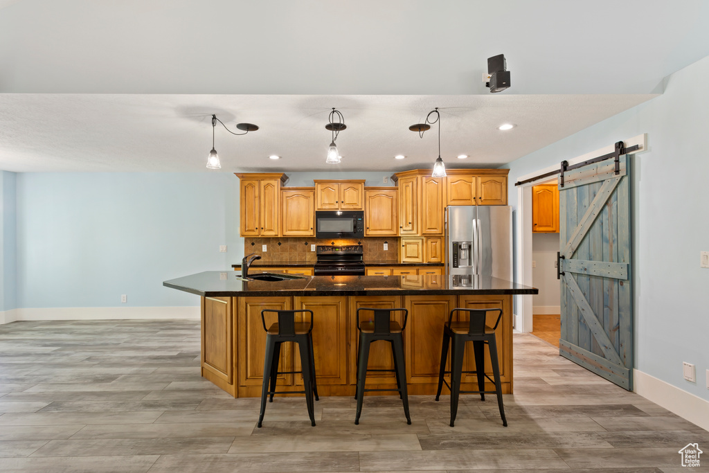 Kitchen featuring a barn door, stainless steel fridge, an island with sink, and range with electric stovetop