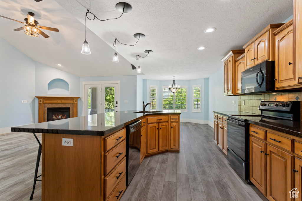 Kitchen featuring black appliances, plenty of natural light, a center island with sink, and hardwood / wood-style floors