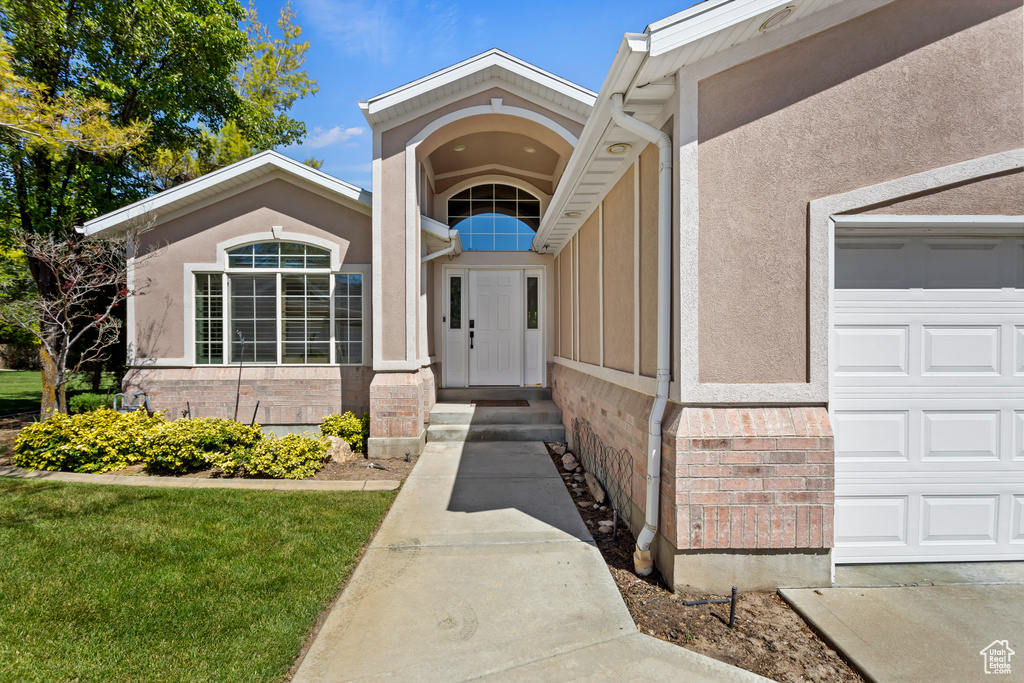 Doorway to property with a garage and a lawn