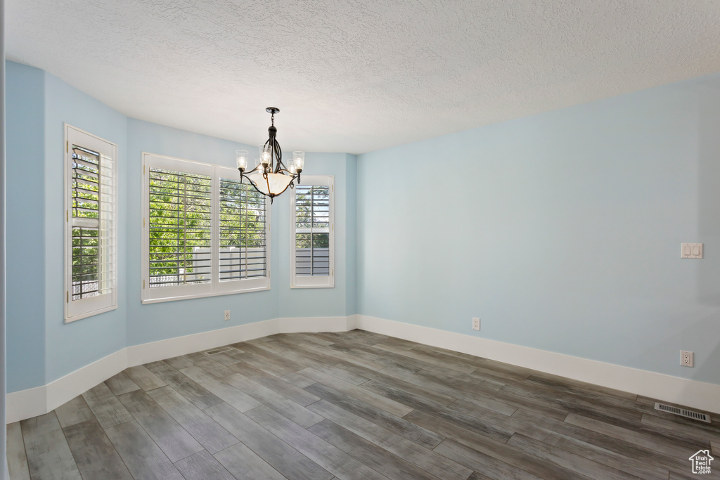 Empty room featuring a chandelier, a textured ceiling, and dark wood-type flooring