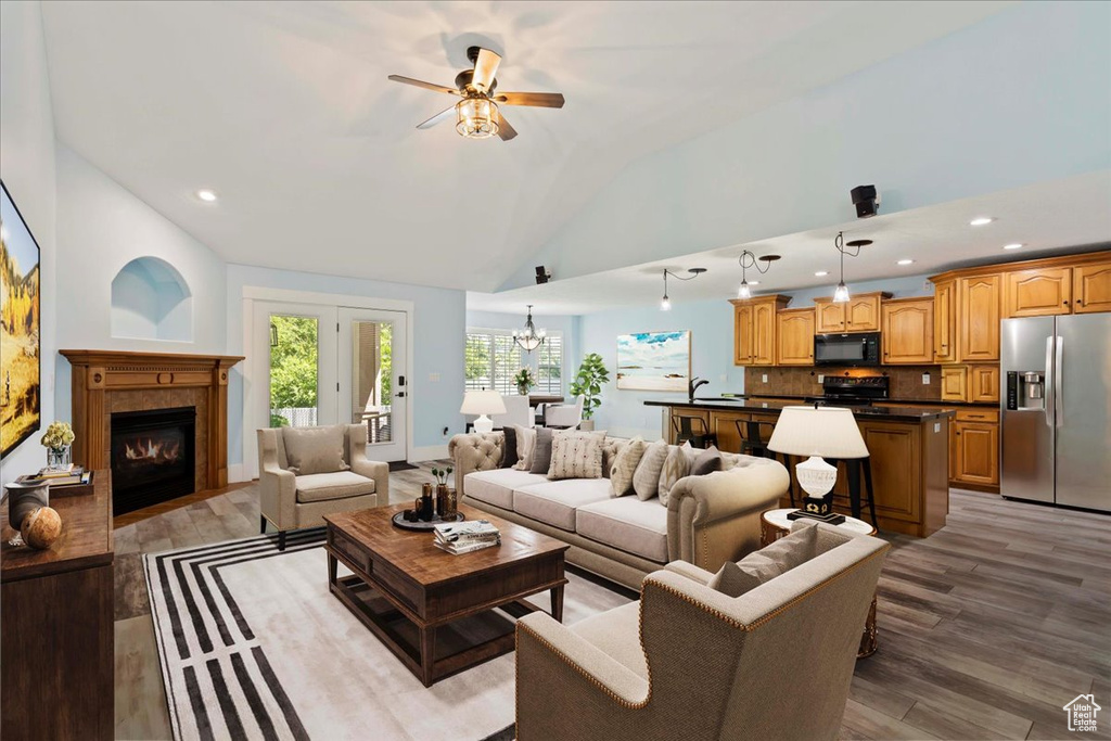 Living room with ceiling fan with notable chandelier, hardwood / wood-style floors, and high vaulted ceiling