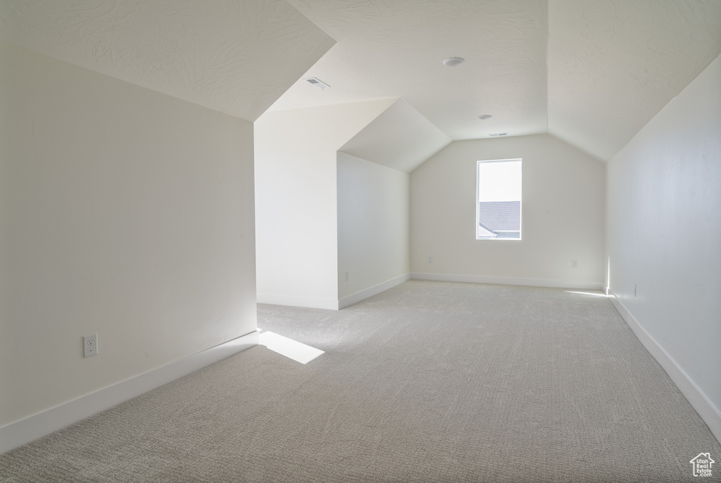 Bonus room with vaulted ceiling and light carpet