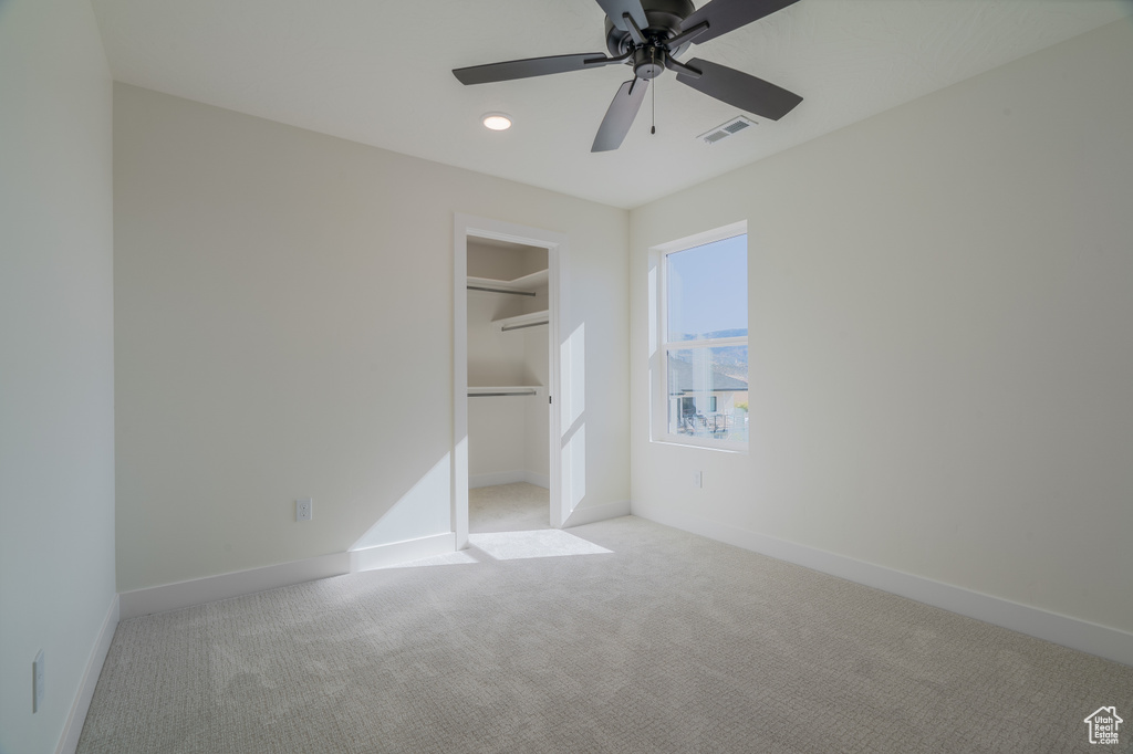 Unfurnished bedroom featuring a spacious closet, ceiling fan, a closet, and light colored carpet