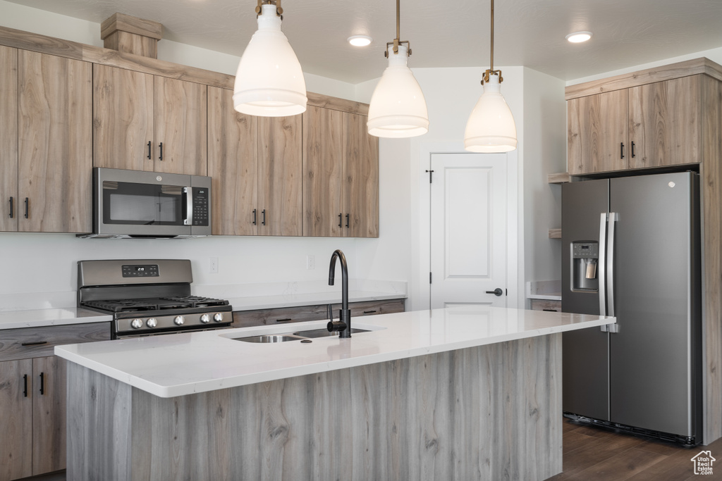 Kitchen with appliances with stainless steel finishes, dark hardwood / wood-style floors, a kitchen island with sink, and pendant lighting