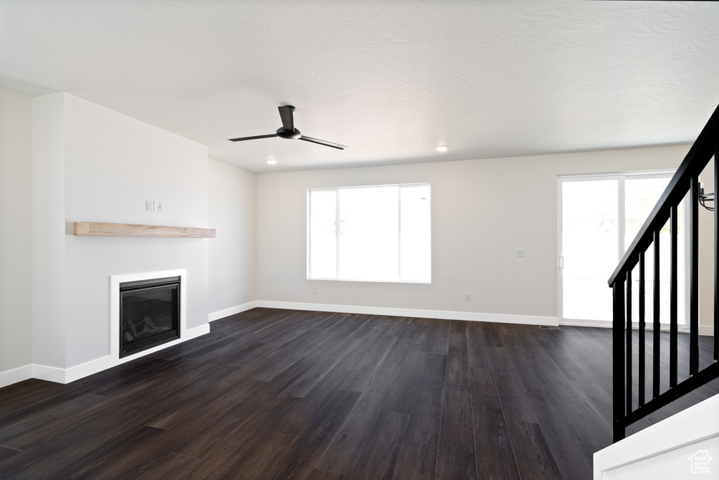 Unfurnished living room featuring a textured ceiling, dark hardwood / wood-style floors, and ceiling fan