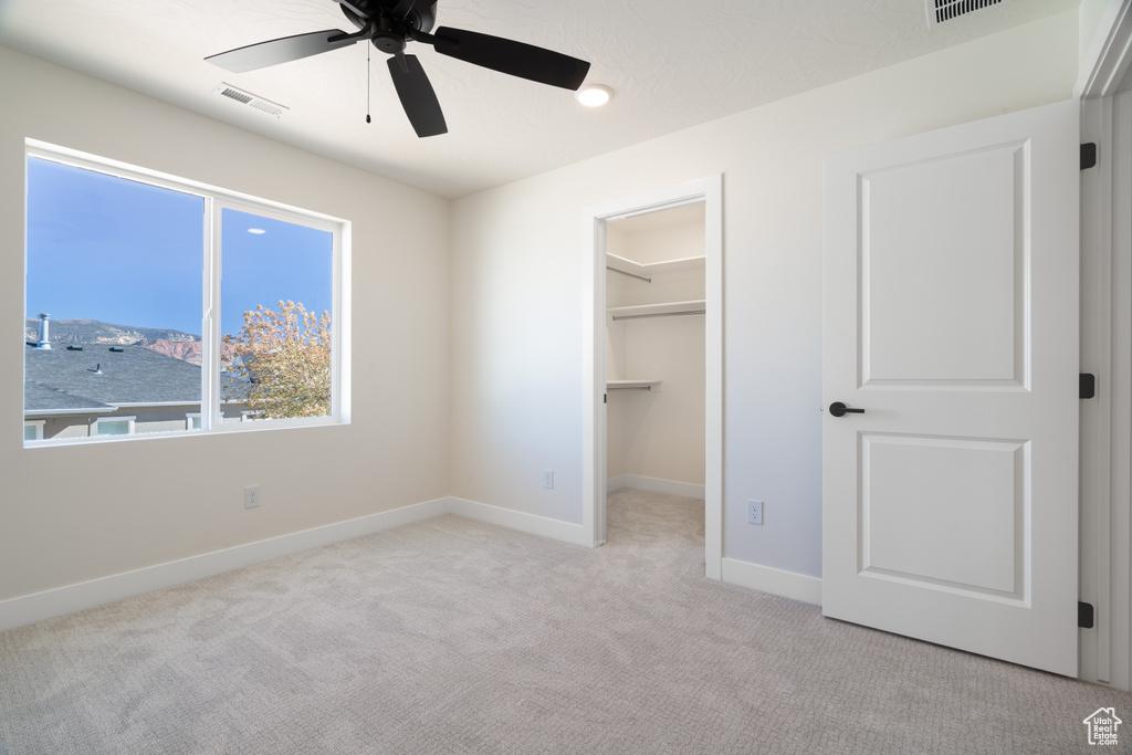 Unfurnished bedroom with light colored carpet, a walk in closet, a closet, and ceiling fan