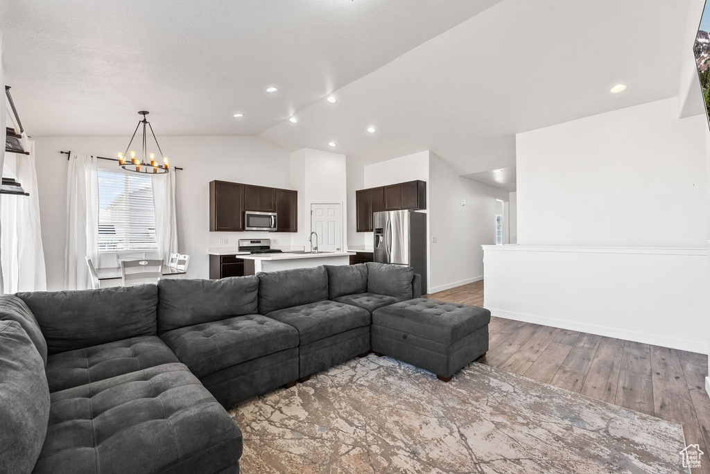 Living room with a notable chandelier, lofted ceiling, sink, and light hardwood / wood-style floors