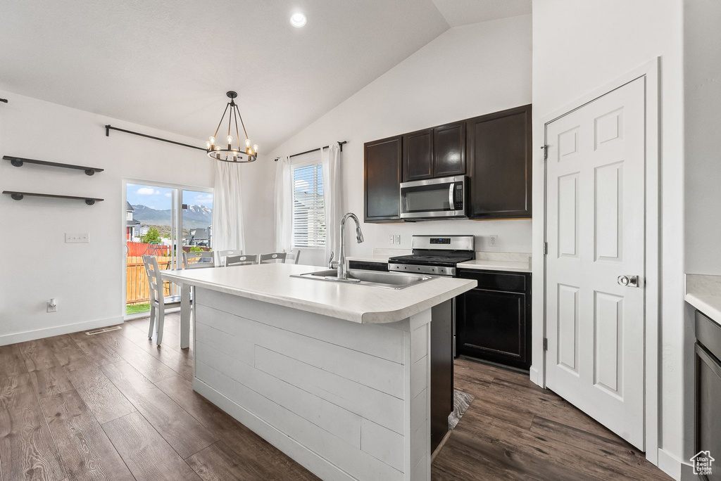 Kitchen with hanging light fixtures, an inviting chandelier, stainless steel appliances, a center island with sink, and dark hardwood / wood-style flooring