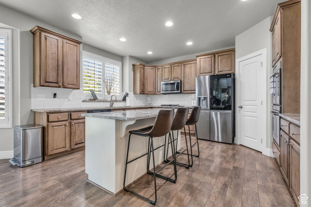 Kitchen with stainless steel appliances, dark hardwood / wood-style flooring, backsplash, and a kitchen island