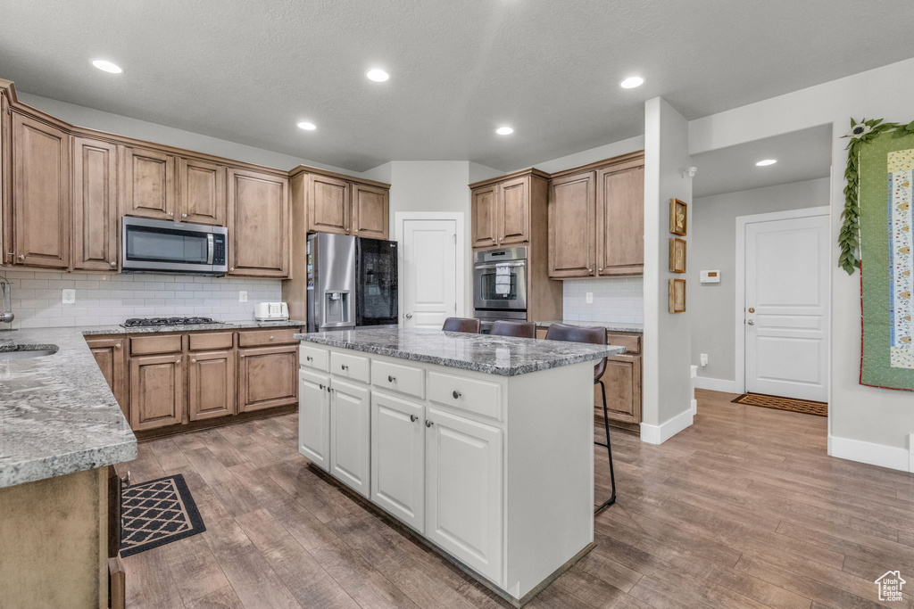 Kitchen with a center island, appliances with stainless steel finishes, white cabinets, hardwood / wood-style floors, and tasteful backsplash