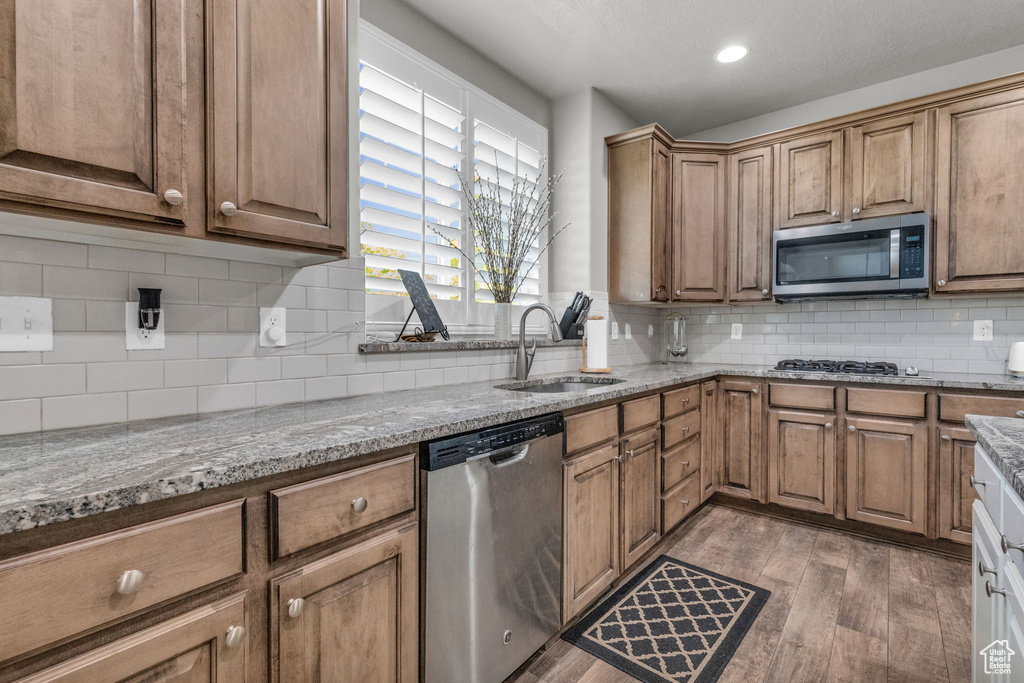 Kitchen featuring appliances with stainless steel finishes, light stone counters, hardwood / wood-style floors, backsplash, and sink