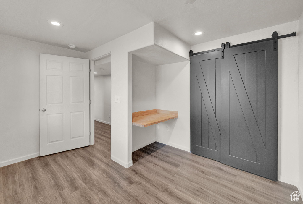 Unfurnished bedroom featuring a barn door and light hardwood / wood-style floors