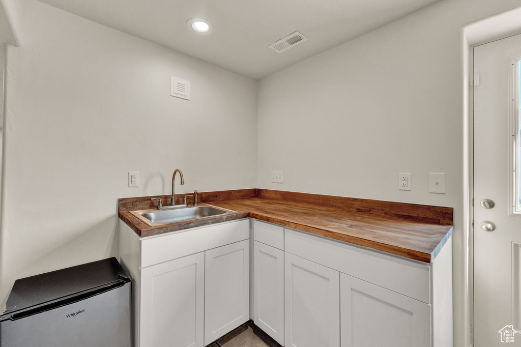 Kitchen featuring sink, white cabinets, wooden counters, and fridge