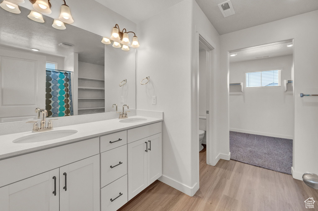 Bathroom featuring toilet, hardwood / wood-style floors, dual sinks, and vanity with extensive cabinet space