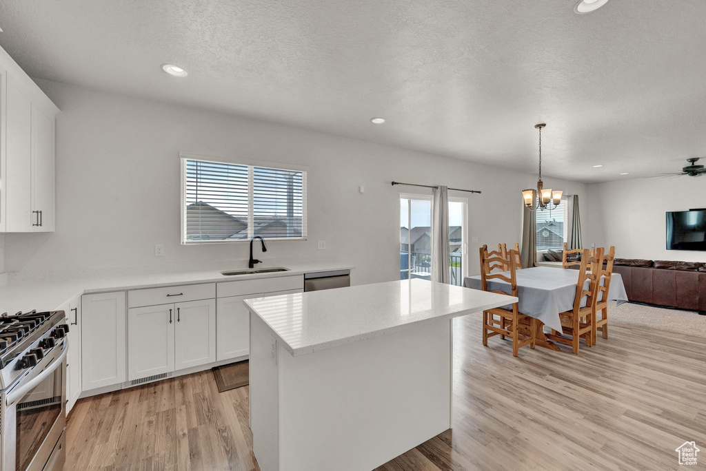 Kitchen with decorative light fixtures, sink, white cabinets, and light hardwood / wood-style flooring