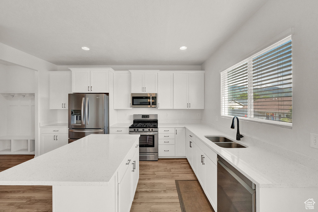 Kitchen with appliances with stainless steel finishes, sink, light hardwood / wood-style flooring, and a kitchen island