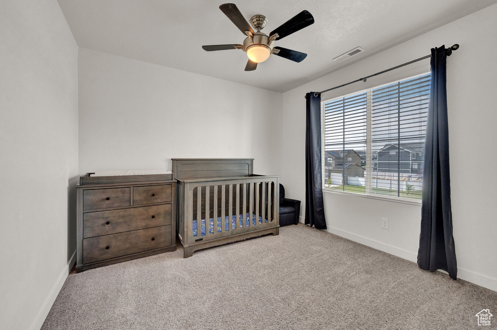 Unfurnished bedroom featuring carpet, ceiling fan, and a crib