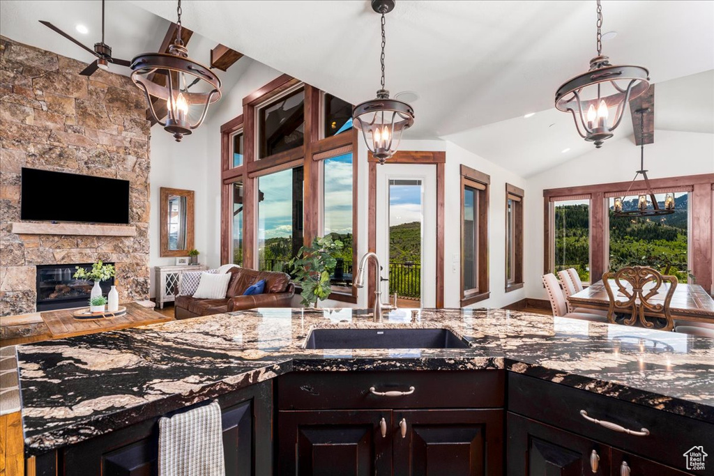 Kitchen featuring hanging light fixtures, a stone fireplace, wood-type flooring, sink, and lofted ceiling