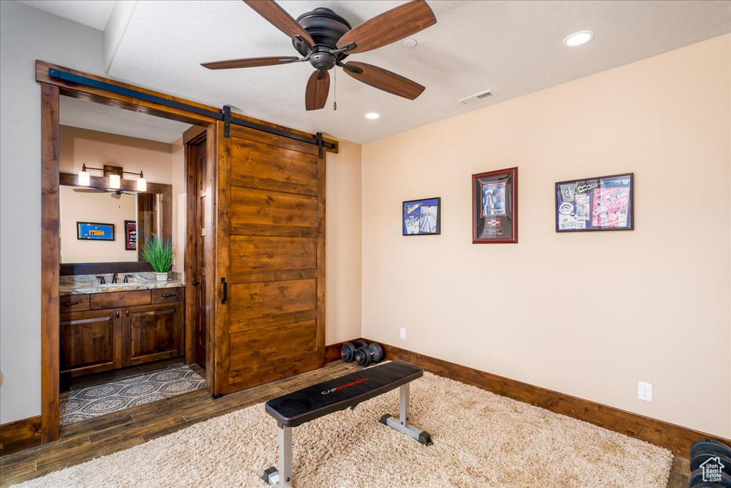 Workout area with a barn door, sink, ceiling fan, and dark hardwood / wood-style flooring