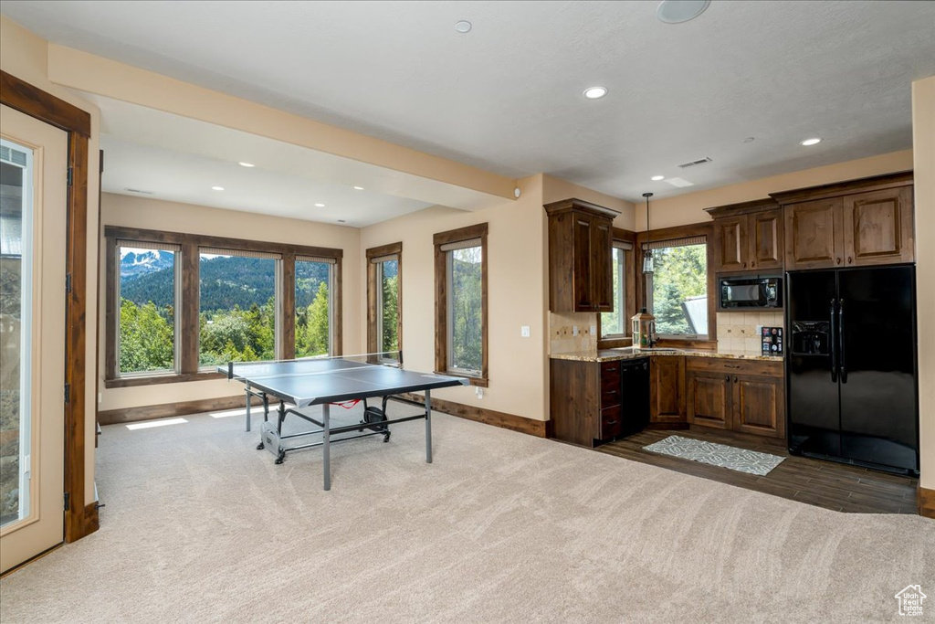 Kitchen featuring light stone counters, tasteful backsplash, black appliances, sink, and carpet floors