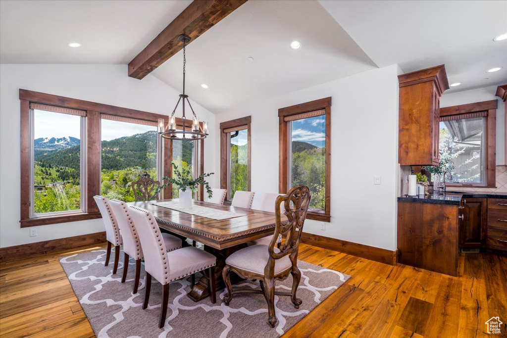 Dining area featuring lofted ceiling with beams, an inviting chandelier, a wealth of natural light, and light wood-type flooring