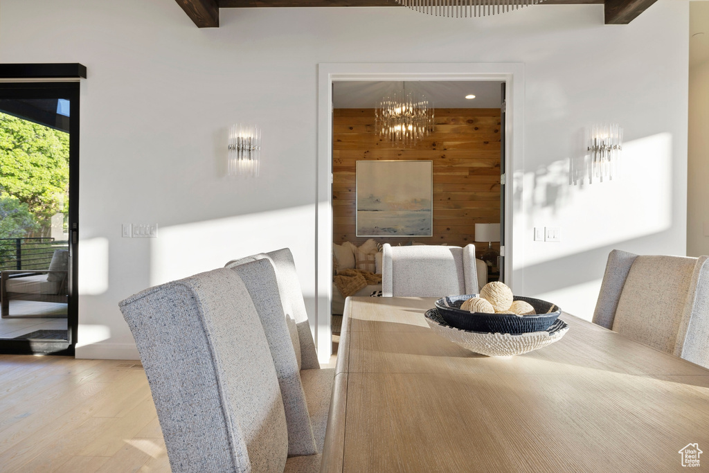 Dining area with beam ceiling, hardwood / wood-style flooring, wood walls, and an inviting chandelier