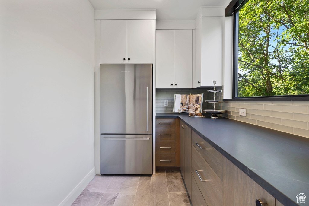 Kitchen with white cabinets, tasteful backsplash, stainless steel refrigerator, and light tile floors