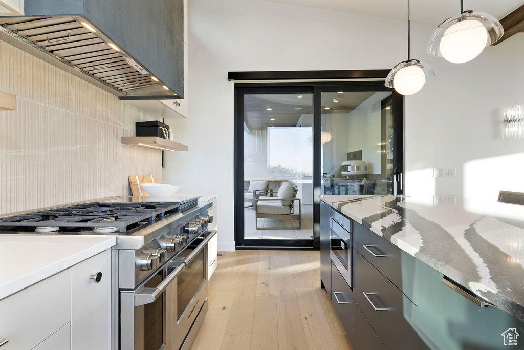 Kitchen with light stone countertops, light hardwood / wood-style floors, wall chimney range hood, range with two ovens, and hanging light fixtures